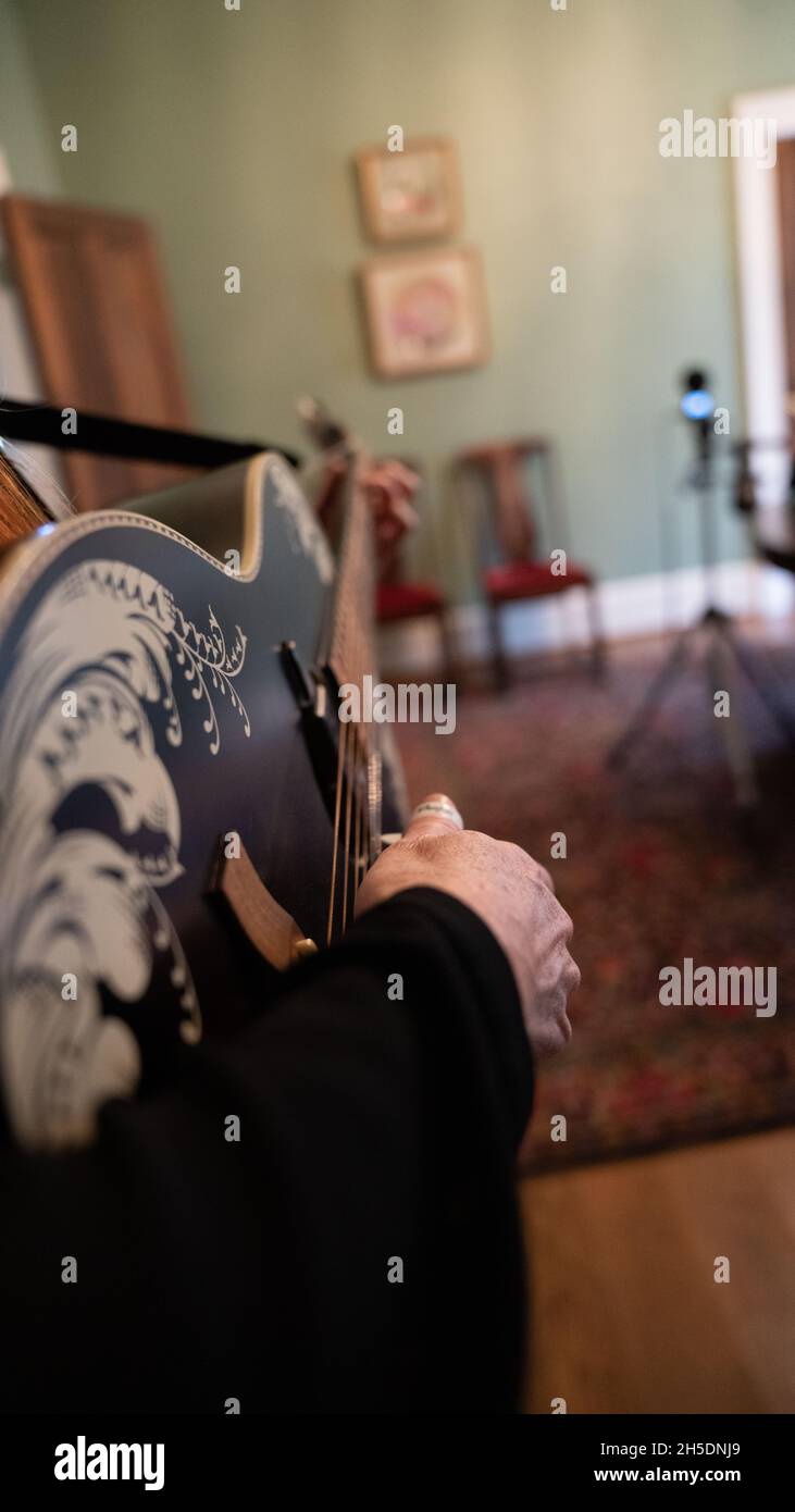 Frau, die die Saiten einer schwarzen Gitarre pflückt - Bild aus nächster Nähe Stockfoto