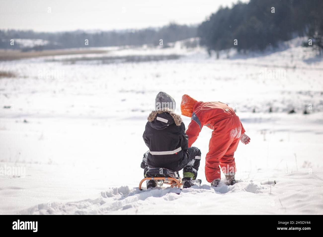 Zwei Jungen besteigen einen verschneiten Berg. Zwei Brüder auf dem Hintergrund einer Winterlandschaft mit einem mit Schnee bedeckten Wald. Extremer Kinderurlaub. Ac Stockfoto