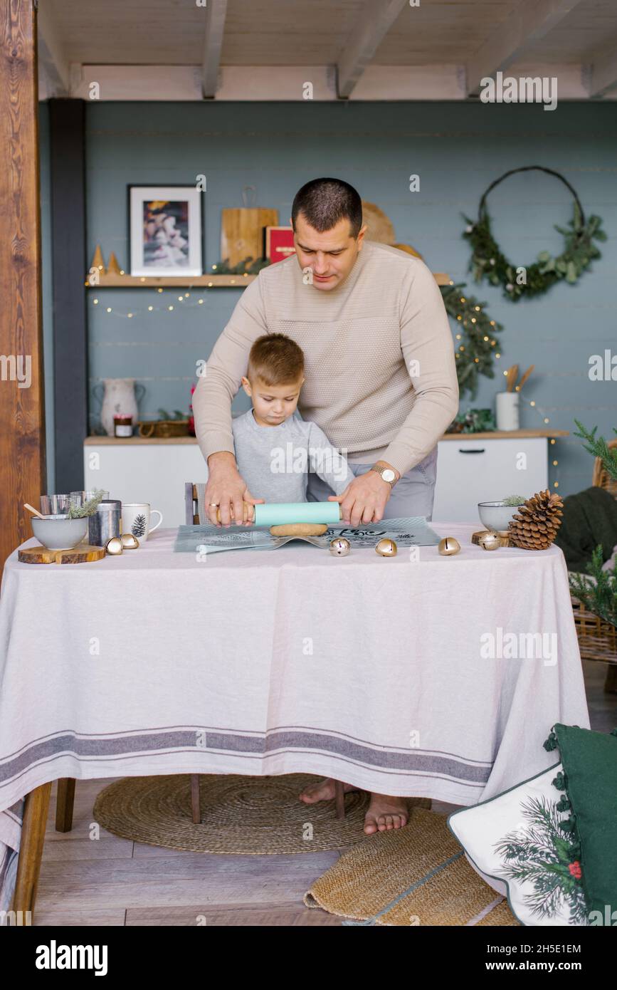 Papa und kleiner Sohn Rollen den Teig in der Küche für Weihnachts-Ingwerkekse oder Lebkuchenhaus aus Stockfoto