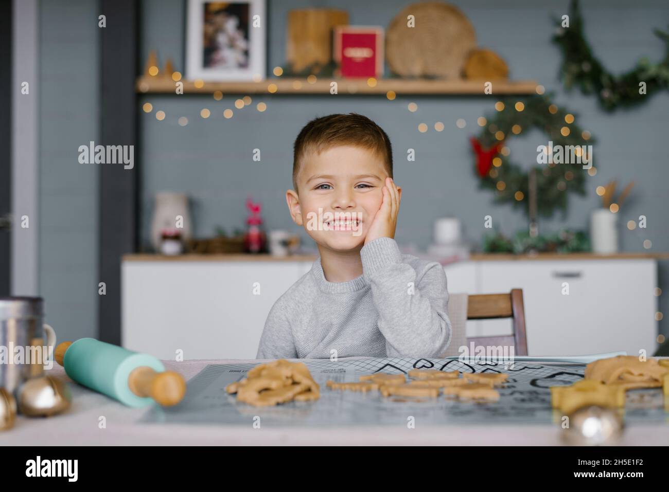 Ein süßer kleiner Junge von 3-4 Jahren sitzt am Tisch und bereitet Weihnachtskekse zu. Familienurlaub zu Hause während der Ferien. Neujahr und Stockfoto