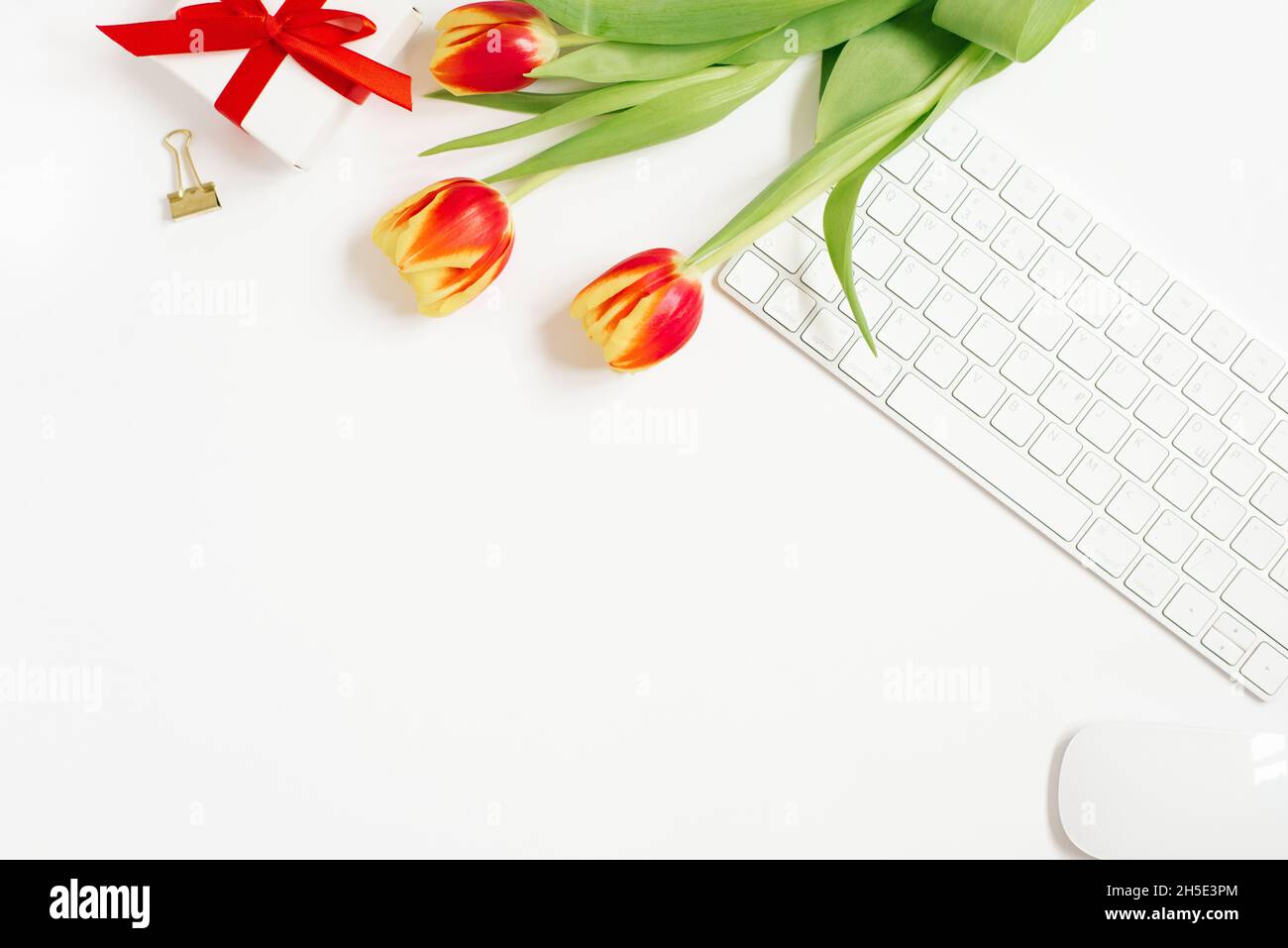 Feminine Komposition aus dem Arbeitsbereich der Frauen, Geschenke zum Muttertag und Valentinstag. Geschenk mit einem roten Band und einem Bouquet von Tulpenblüten, Keyboar Stockfoto