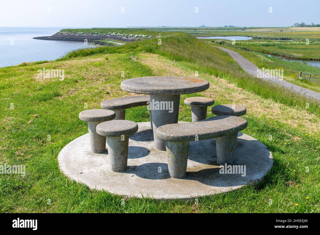 Panoramablick über den Deich bei Oosterend auf der niederländischen Insel Texel mit Küstenlinie, Feuchtgebieten und im Vordergrund auf dem Deich ein Beton Stockfoto