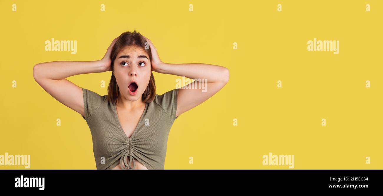 Flyer mit schockiertem jungen Mädchen, Student, der mit offenem Mund steht und isoliert auf gelbem Studiohintergrund schreit. Stockfoto