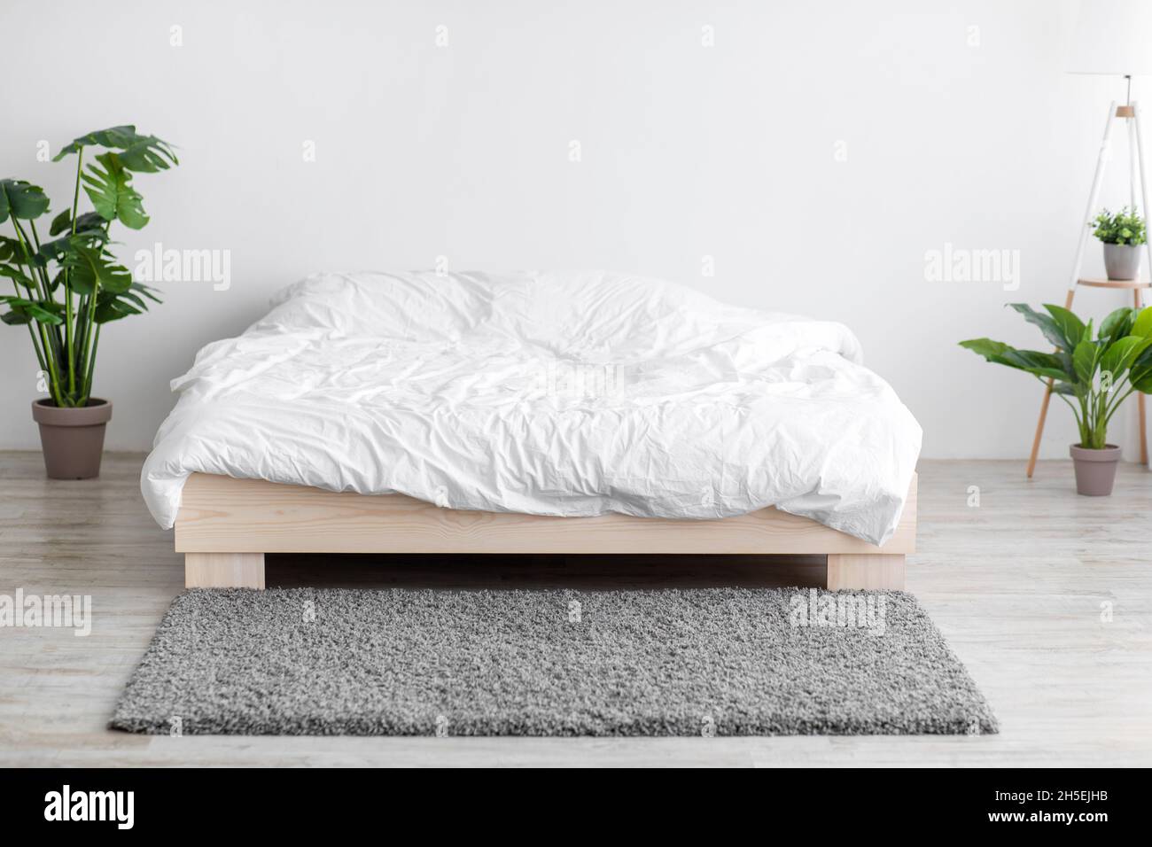 Komfortables Doppelbett mit Bettwäsche, weichem grauem Teppich und Topfpflanzen auf dem Boden Stockfoto