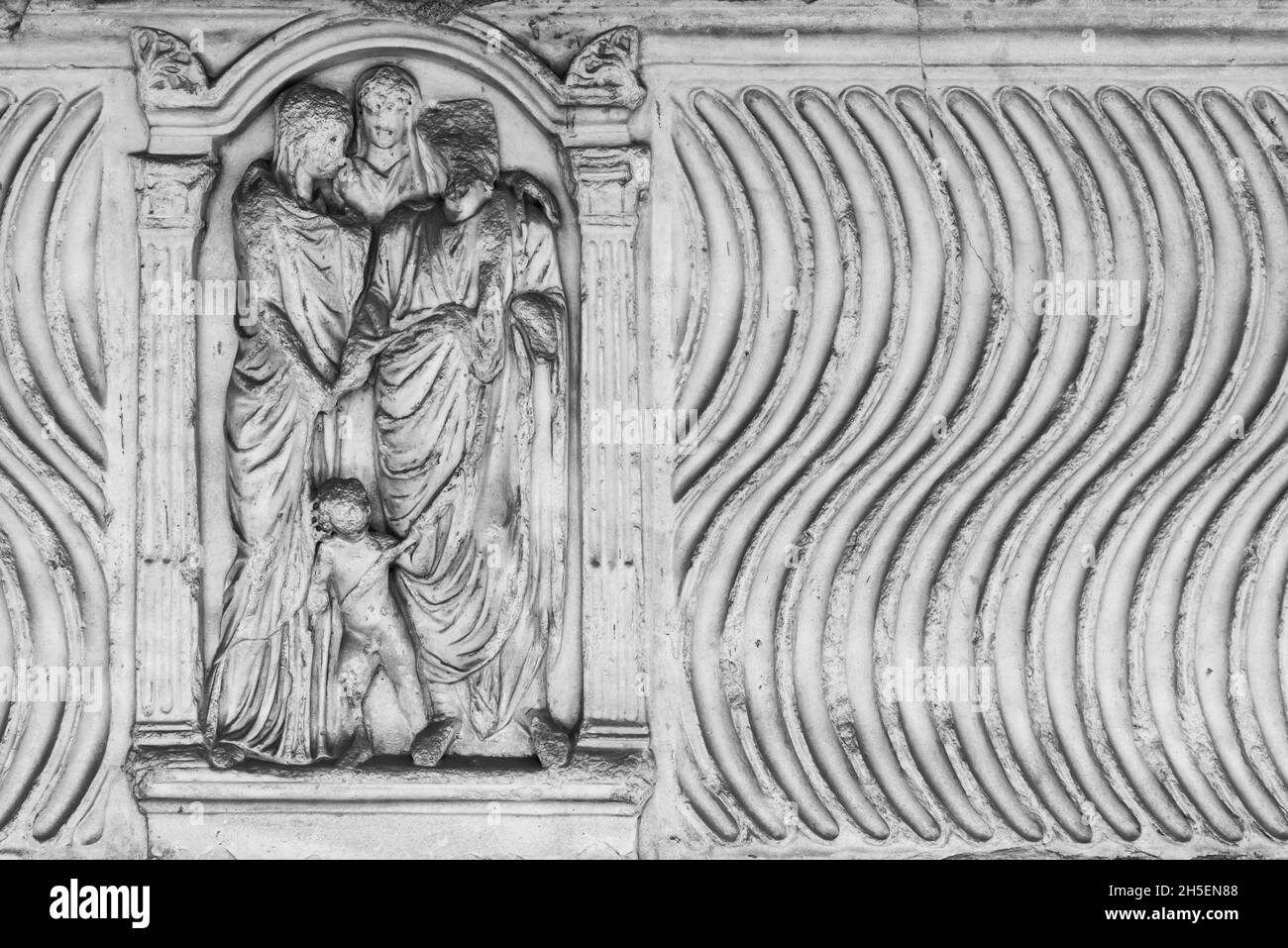Schwarz-weißes Foto von antiken Skulpturen, die auf einer Marmorwand geschnitzt sind und eine Gruppe römischer Frauen darstellen, die mit einem Kind vereint wurden Stockfoto