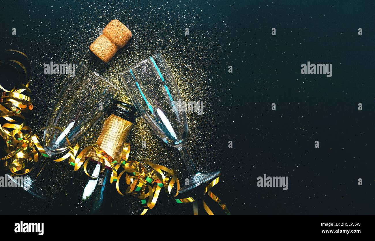 Frohes neues Jahr. Champagnerflasche mit zwei Gläsern, goldenen Luftschlangen und funkelndem Glitzer mit Kopierraum auf schwarzem Hintergrund. Silvesterfeier Stockfoto