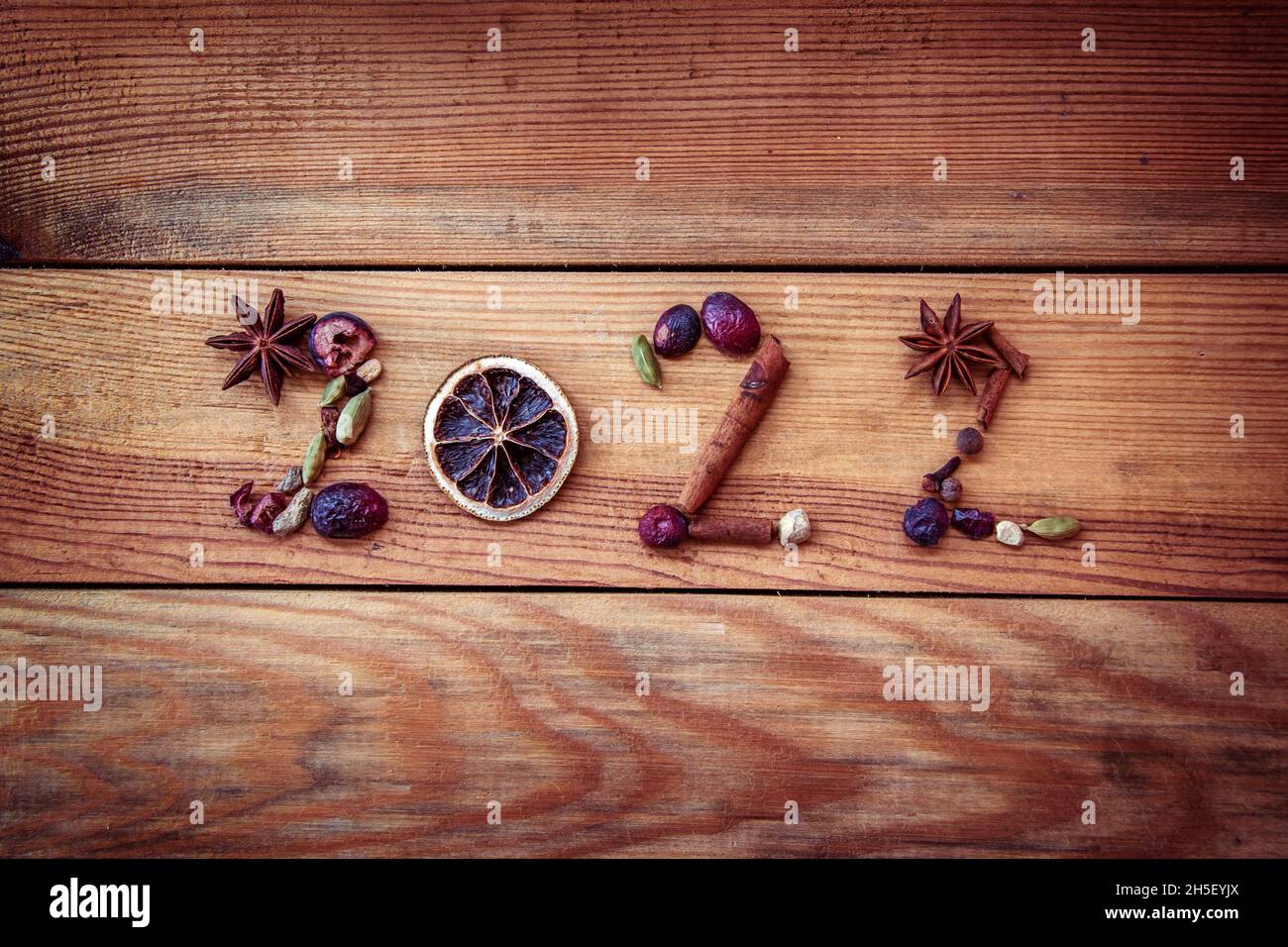 2022 geschrieben mit weihnachtlichen Gewürzen und getrockneten Früchten auf Holzhintergrund, Neujahr Grußkarte Stockfoto