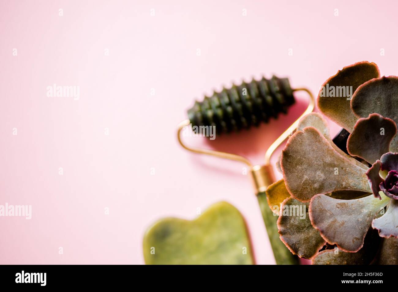 Jade Roller und Gesichtsmassage Scrubber auf einem weichen rosa Hintergrund. Stockfoto