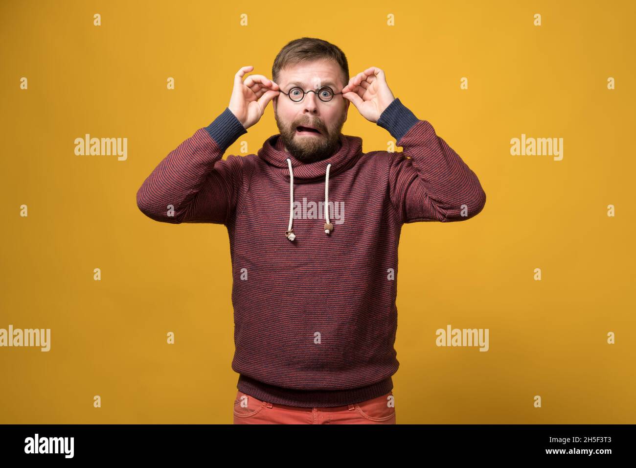 Lustiger kaukasischer bärtiger Mann setzte einen Spielzeugrand aus Gläsern ohne Linsen auf und machte eine bizarre Grimasse. Gelber Hintergrund. Stockfoto