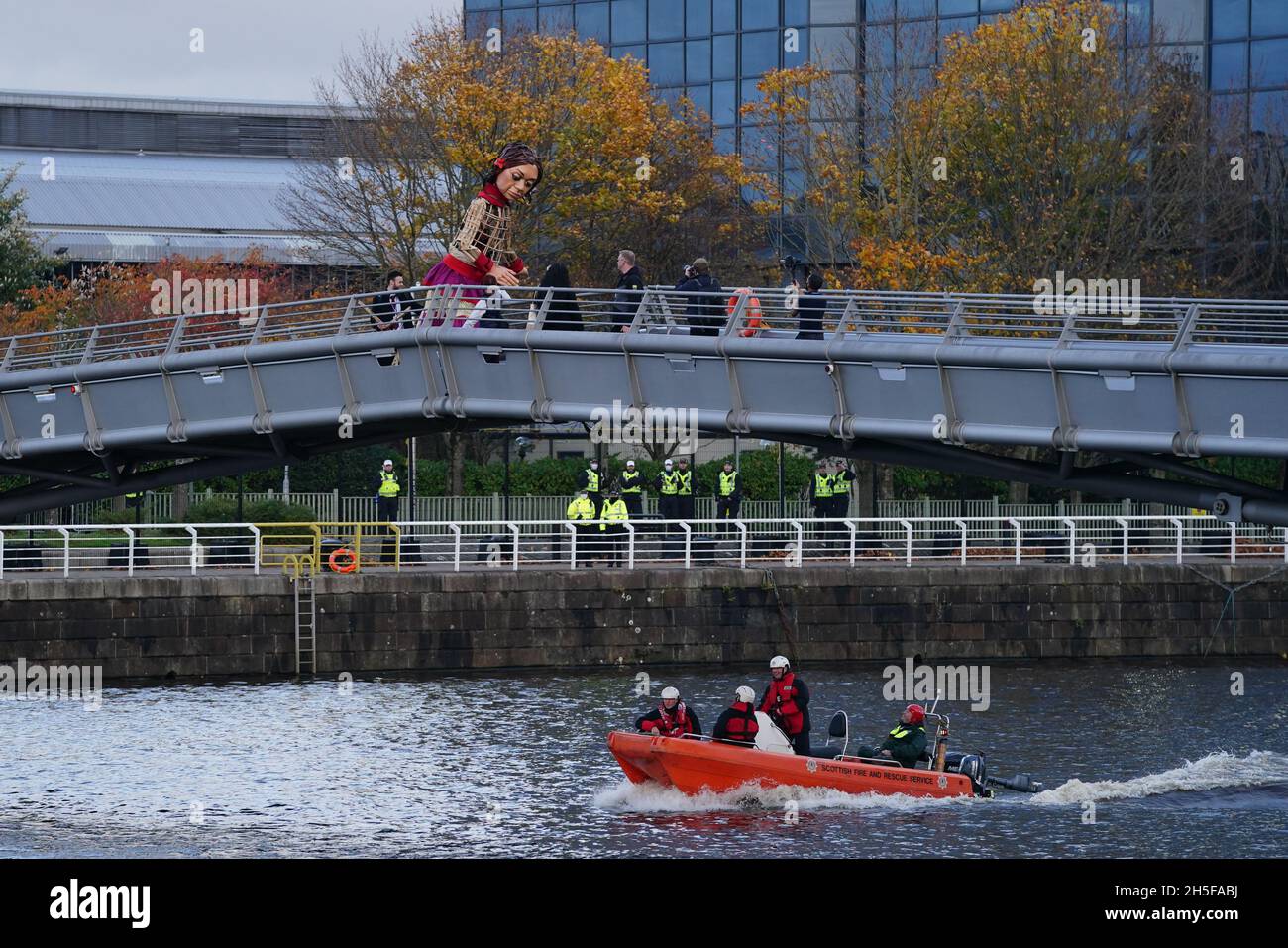 Puppet Little Amal geht über den Fluss Clyde in Glasgow zum Ufer des Cop26-Gipfels Green Zone mit jungen Aktivisten und Mitgliedern der JUGENDLICHEN DER MAPA (am stärksten betroffene Menschen und Gebiete). Die 3.5 Meter große Marionette eines 10-jährigen syrischen Flüchtlings begann ihre Reise in der Türkei am 27. Juli und hat fast 8,000 km durch Griechenland, Italien, Deutschland, die Schweiz, Belgien und Frankreich gereist, Symbolisiert Millionen von vertriebenen Kindern. Bilddatum: Dienstag, 9. November 2021. Stockfoto