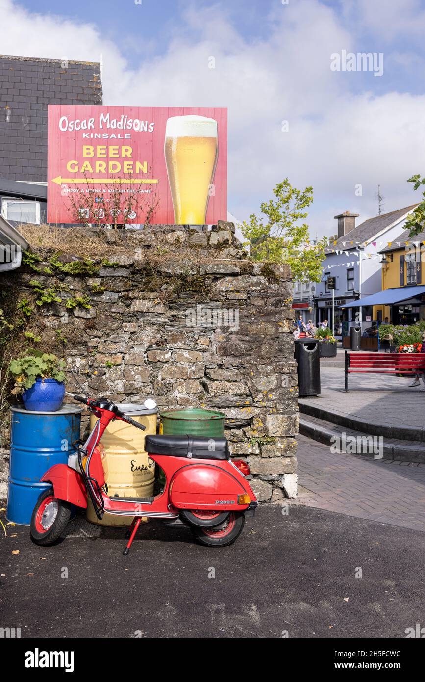 Roller Red Vespa P200E, geparkt an Metallfässern und Steinmauer in Kinsale, County Cork, Irland Stockfoto