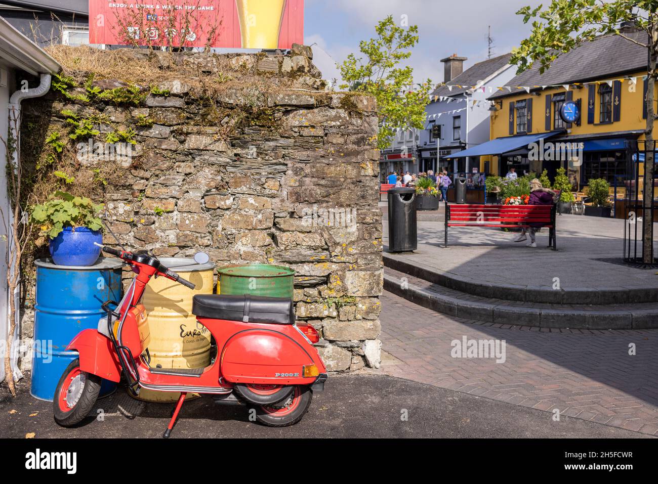 Roller Red Vespa P200E, geparkt an Metallfässern und Steinmauer in Kinsale, County Cork, Irland Stockfoto
