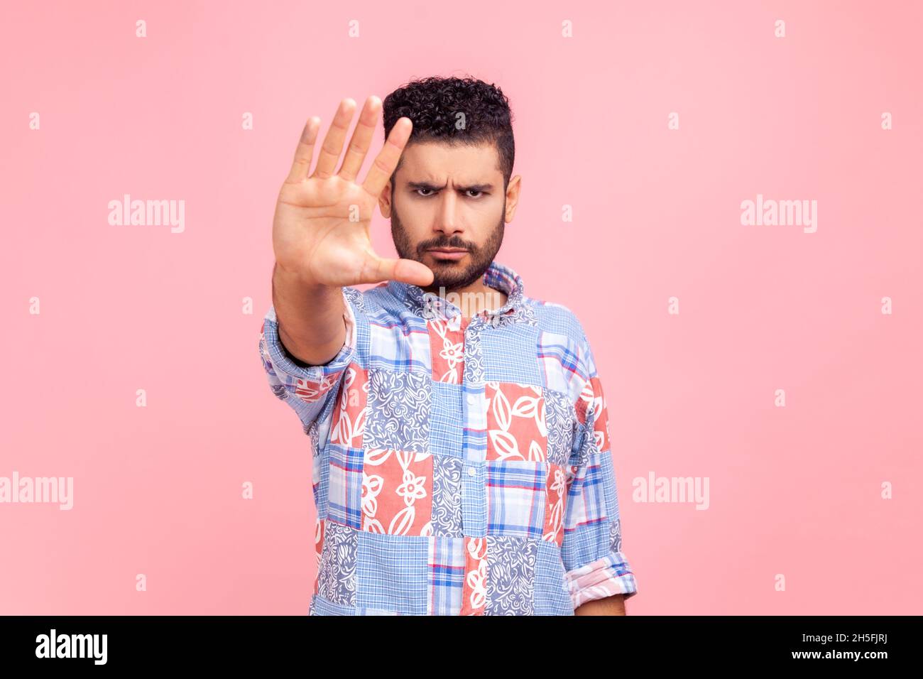 Strenger brünett bärtiger Mann mit Stoppschild vor der Kamera, trägt einen legeren blauen Anzug, der mit runzelndem Gesicht und herrischem Ausdruck steht. Innenaufnahme des Studios isoliert auf rosa Hintergrund. Stockfoto