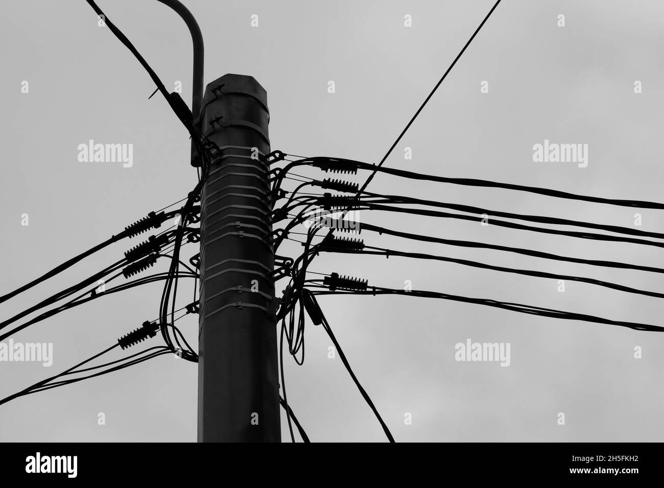 Spitze eines Mastes mit Stromkabeln unter bewölktem Himmel, schwarz-weißes Industriefoto Stockfoto