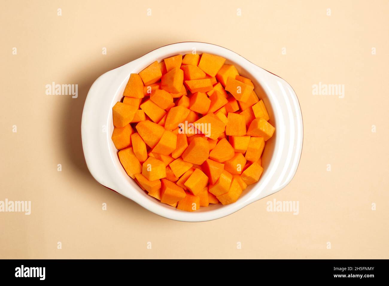 Gehackte Kürbisstücke in einem Topf Draufsicht. Gesundes Lebensmittelkonzept. Flache Utensilien zum Kochen auf beigefarbenem Hintergrund Stockfoto