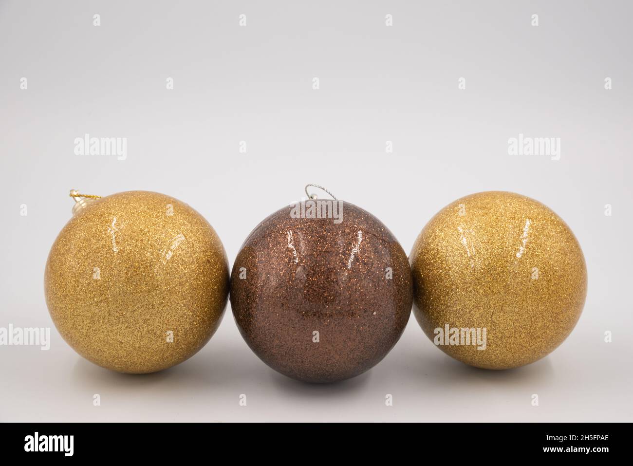 Linie aus zwei goldenen und einer braunen Weihnachtskugeln isoliert auf weißem Hintergrund. Stockfoto