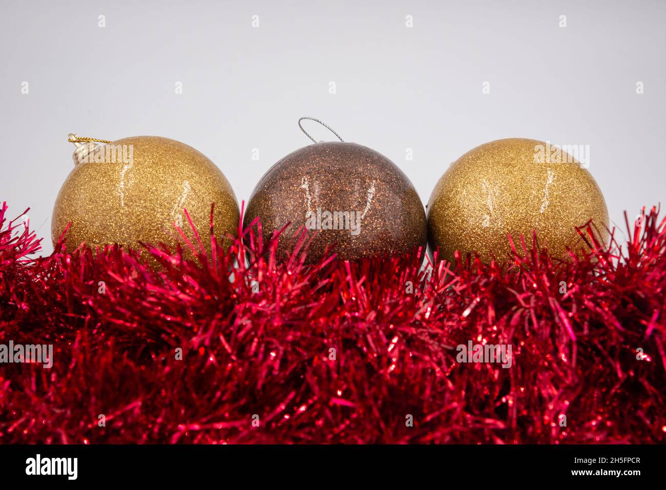 Linie aus zwei goldenen und einer braunen Weihnachtskugeln mit rotem Lametta vorne isoliert auf weißem Hintergrund. Stockfoto