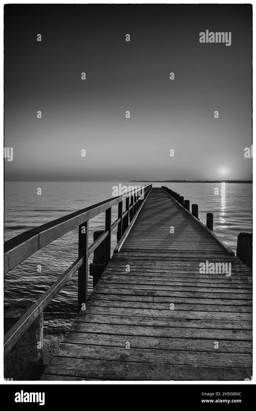 Vertikale Graustufenaufnahme des Sonnenaufgangs über dem Meer. Travemunde. Stockfoto