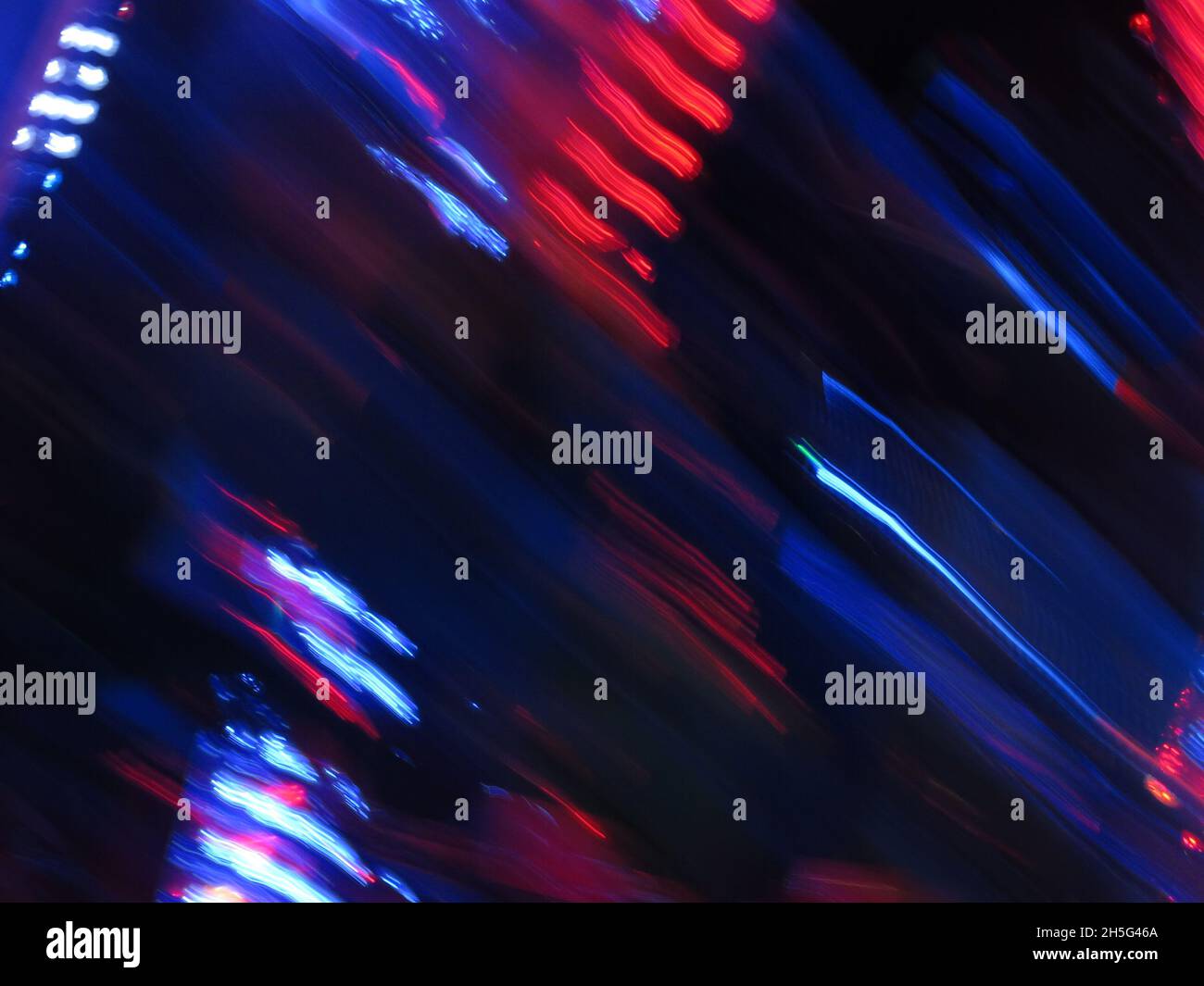 Rote und blaue Lichtwege am Nachthimmel von einem sich drehenden Festplatz, der von hellen Lichterketten bedeckt ist. Stockfoto