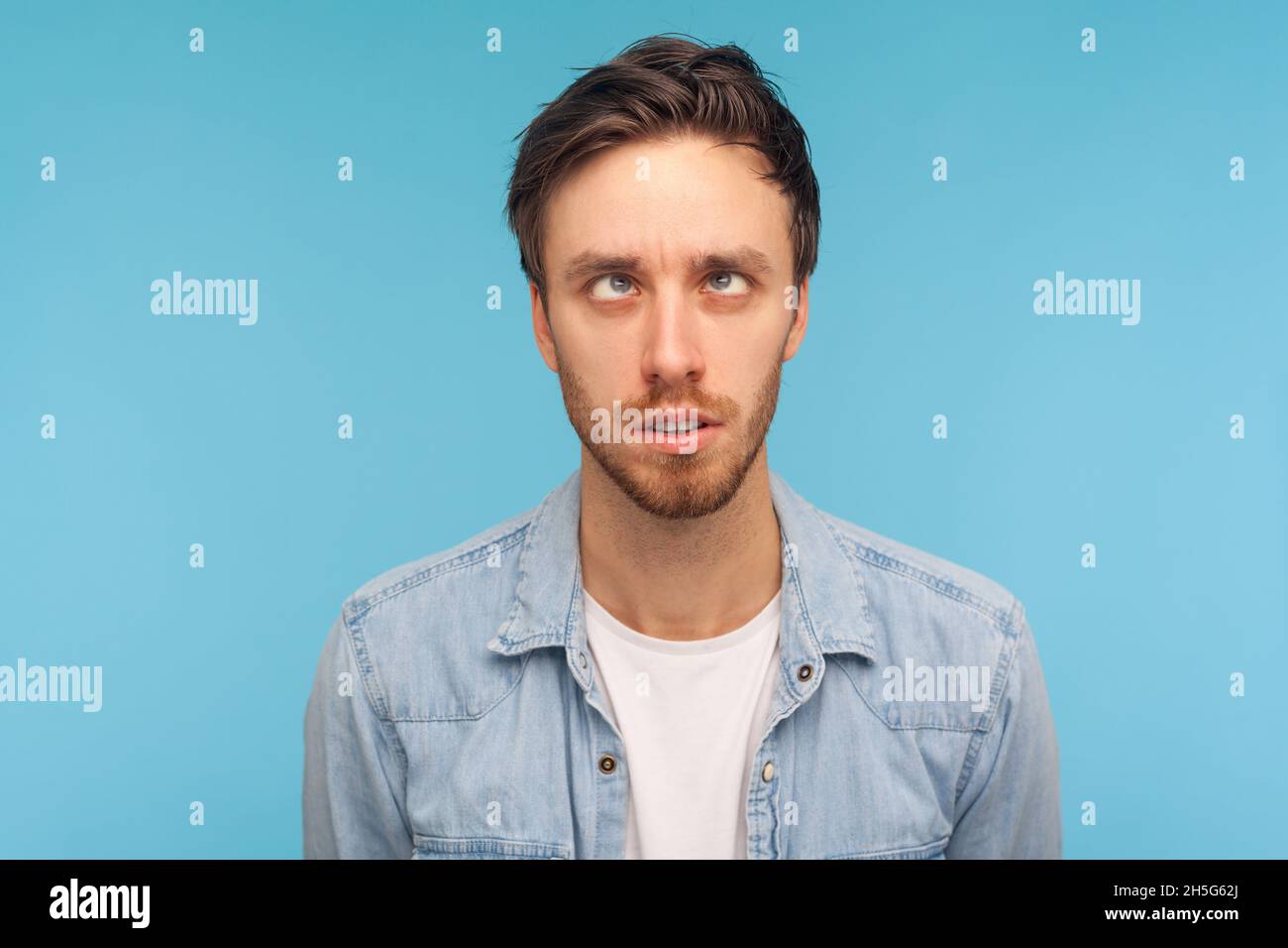 Porträt eines komischen positiven, gutaussehenden Mannes, der Denim-Hemd trägt, mit gekreuzte Augen aussieht, Spaß mit albernem Gesichtsausdruck hat, Narr spielt. Innenaufnahme des Studios isoliert auf blauem Hintergrund. Stockfoto