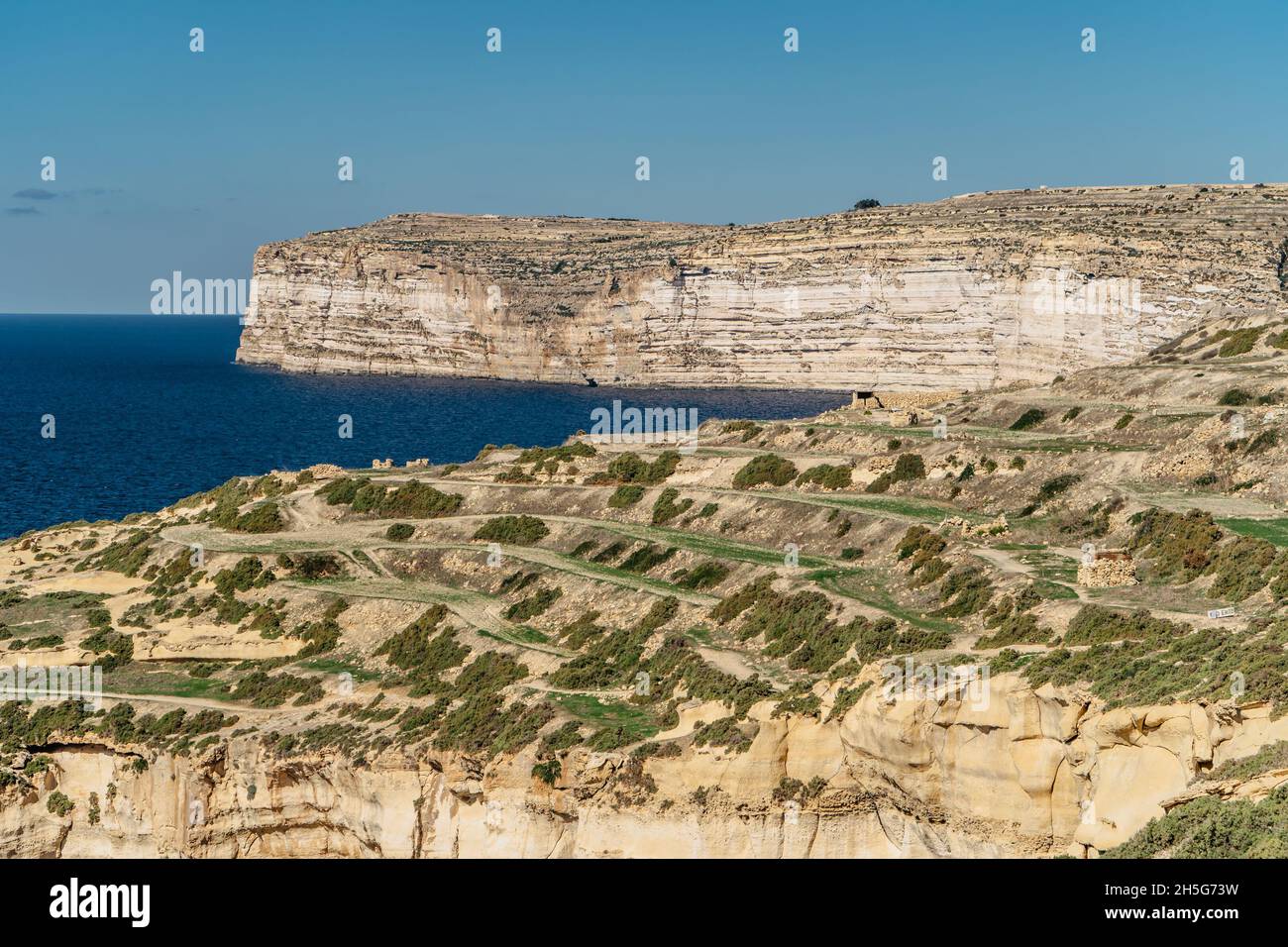 Felsige Kalksteinküste der Insel Gozo und Mittelmeer mit türkisblauem Wasser und Höhlen. Grüne terrassenförmige Felder, Hügel. Beliebte Wanderklippen Stockfoto