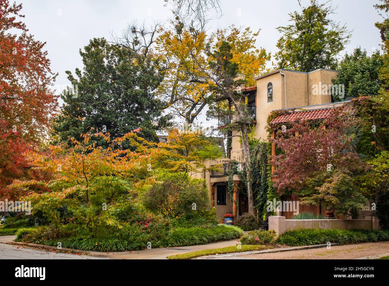 Haus, das wie eine italienische Villa aussieht, mit Balkonen und rotem Ziegeldach mit üppigem Herbstlaub, das an bewölktem Tag Farben färbt - gesättigt Stockfoto