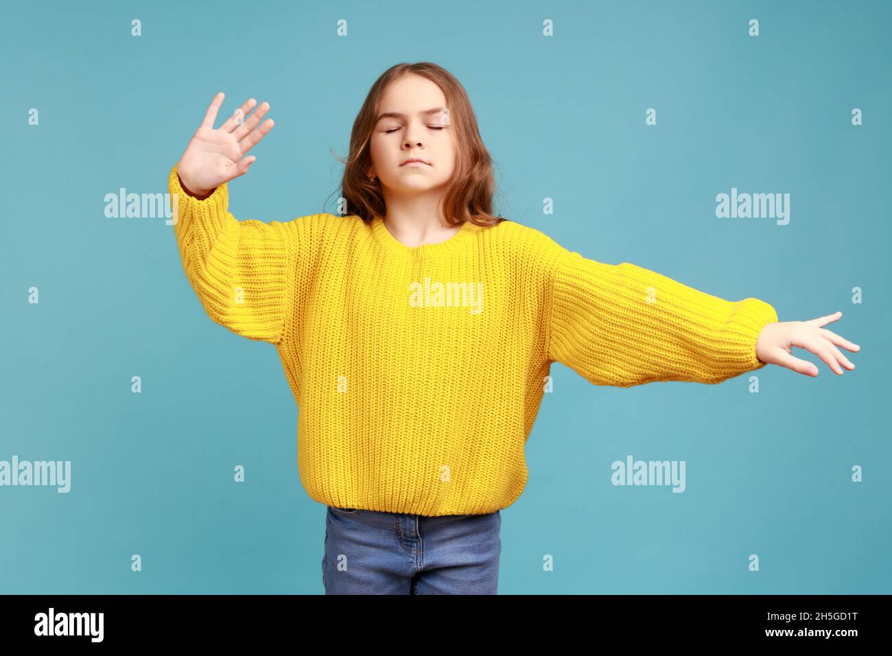 Portrait of cute Little girl Walking blind mit geschlossenen Augen und ausgestreckten Händen, Suchweg, tragen gelben lässigen Stil Pullover. Innenaufnahme des Studios isoliert auf blauem Hintergrund. Stockfoto