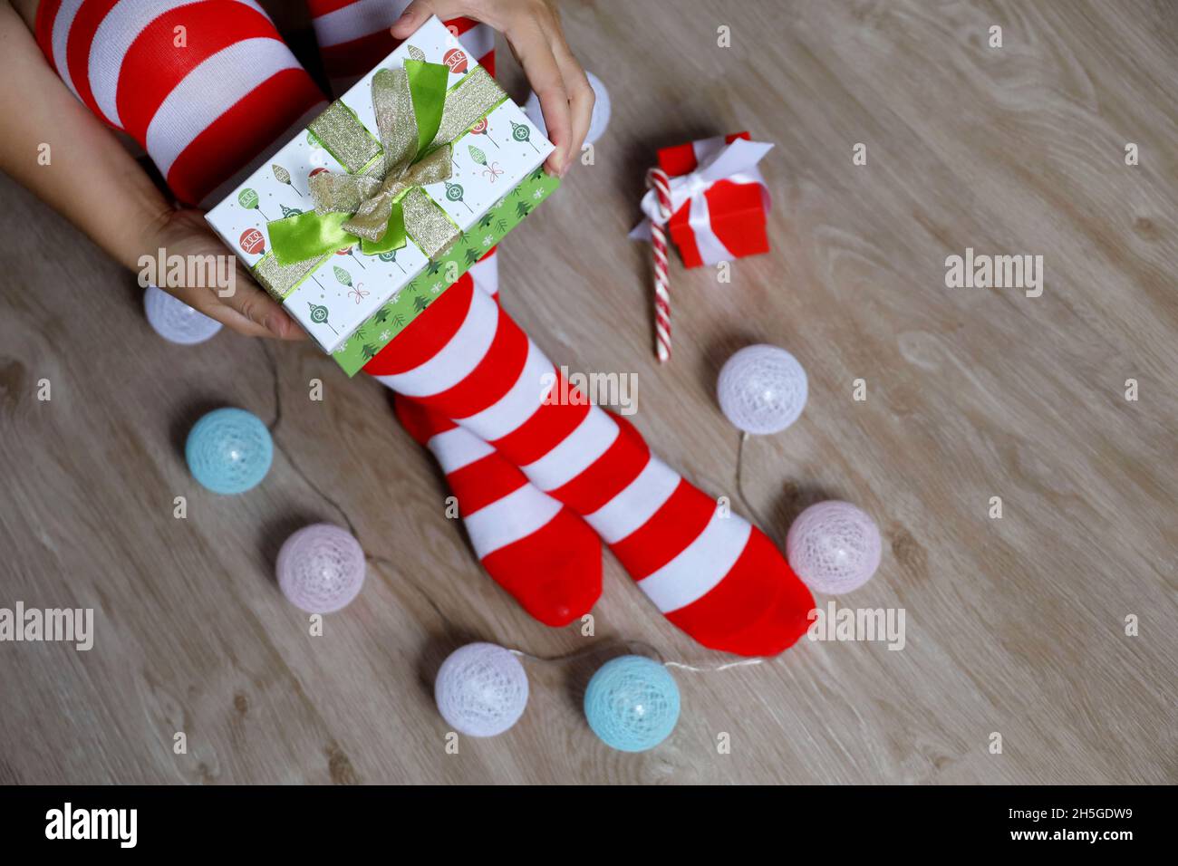 Frau in Weihnachtskniesocken öffnen die Geschenkbox auf einem Boden sitzend, Neujahrsfeier Stockfoto