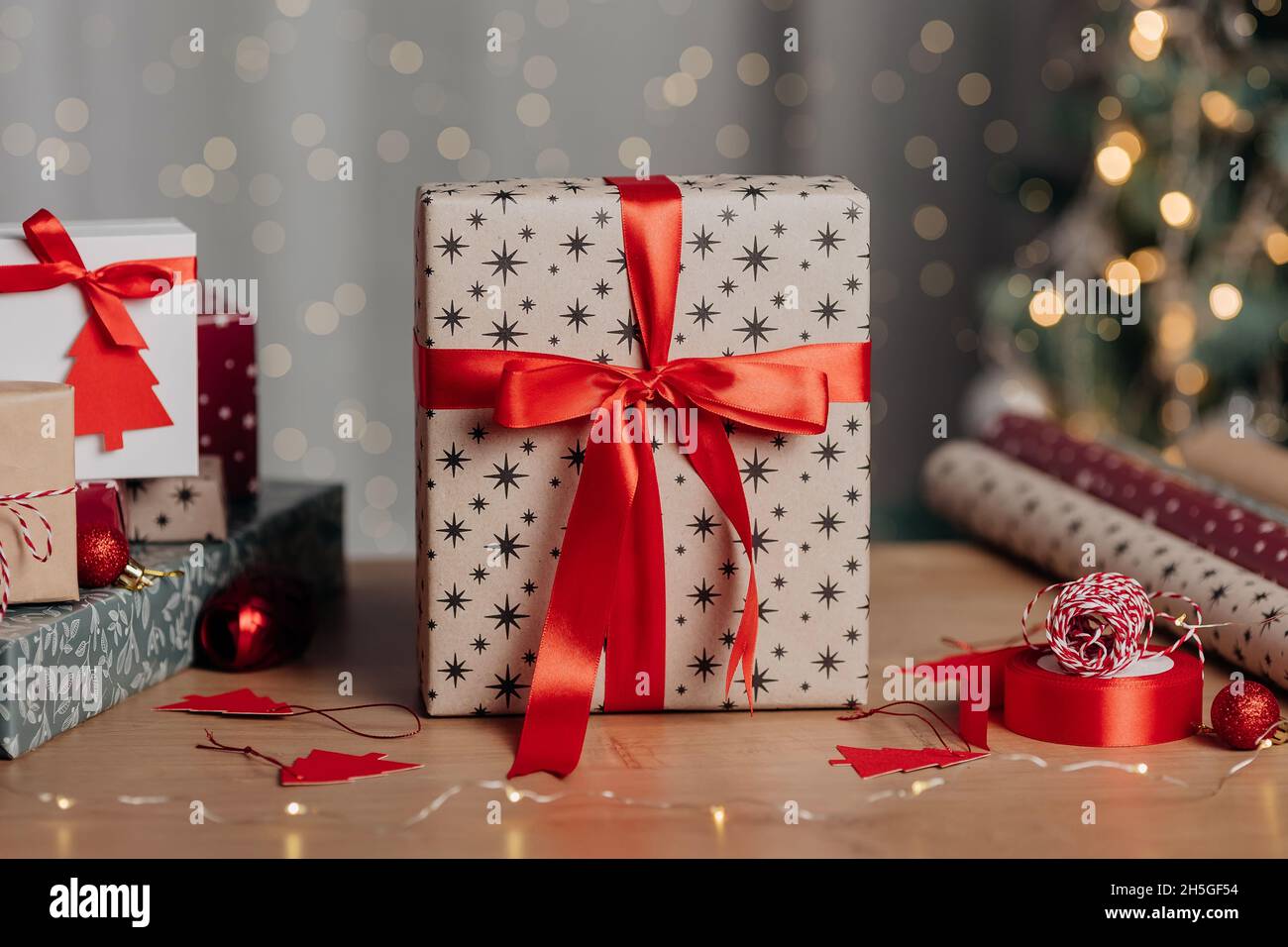 Schöne Weihnachts-Geschenkbox in Kraftpapier und rotem Band auf dem Hintergrund von weihnachtsbaum und Lichter eingewickelt. Präsentiert die Vorbereitung Stockfoto