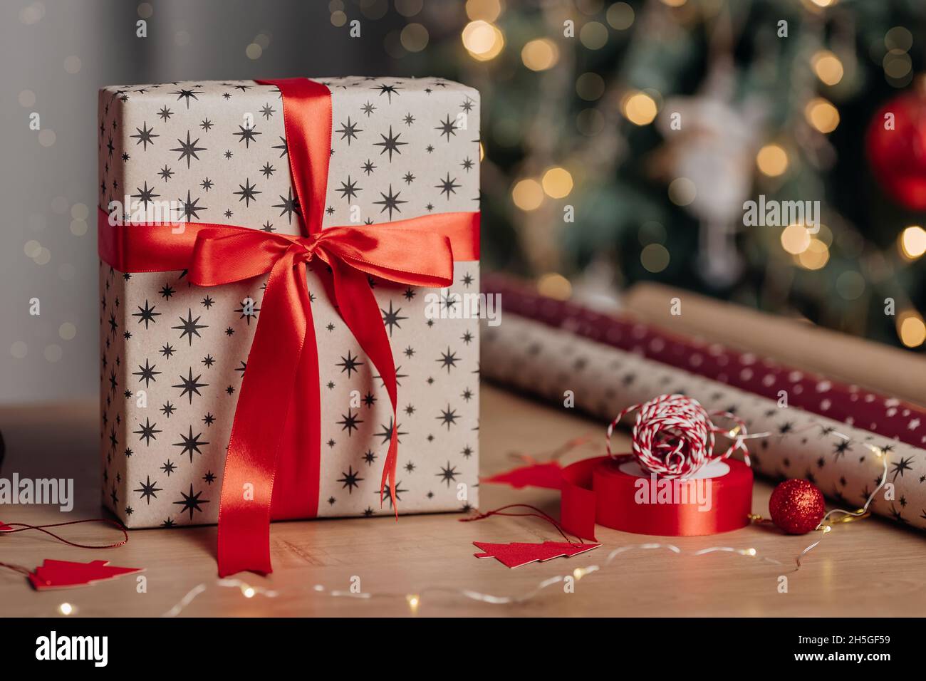 Schöne Weihnachts-Geschenkbox in Kraftpapier und rotem Band auf dem Hintergrund von weihnachtsbaum und Lichter eingewickelt. Präsentiert die Vorbereitung Stockfoto