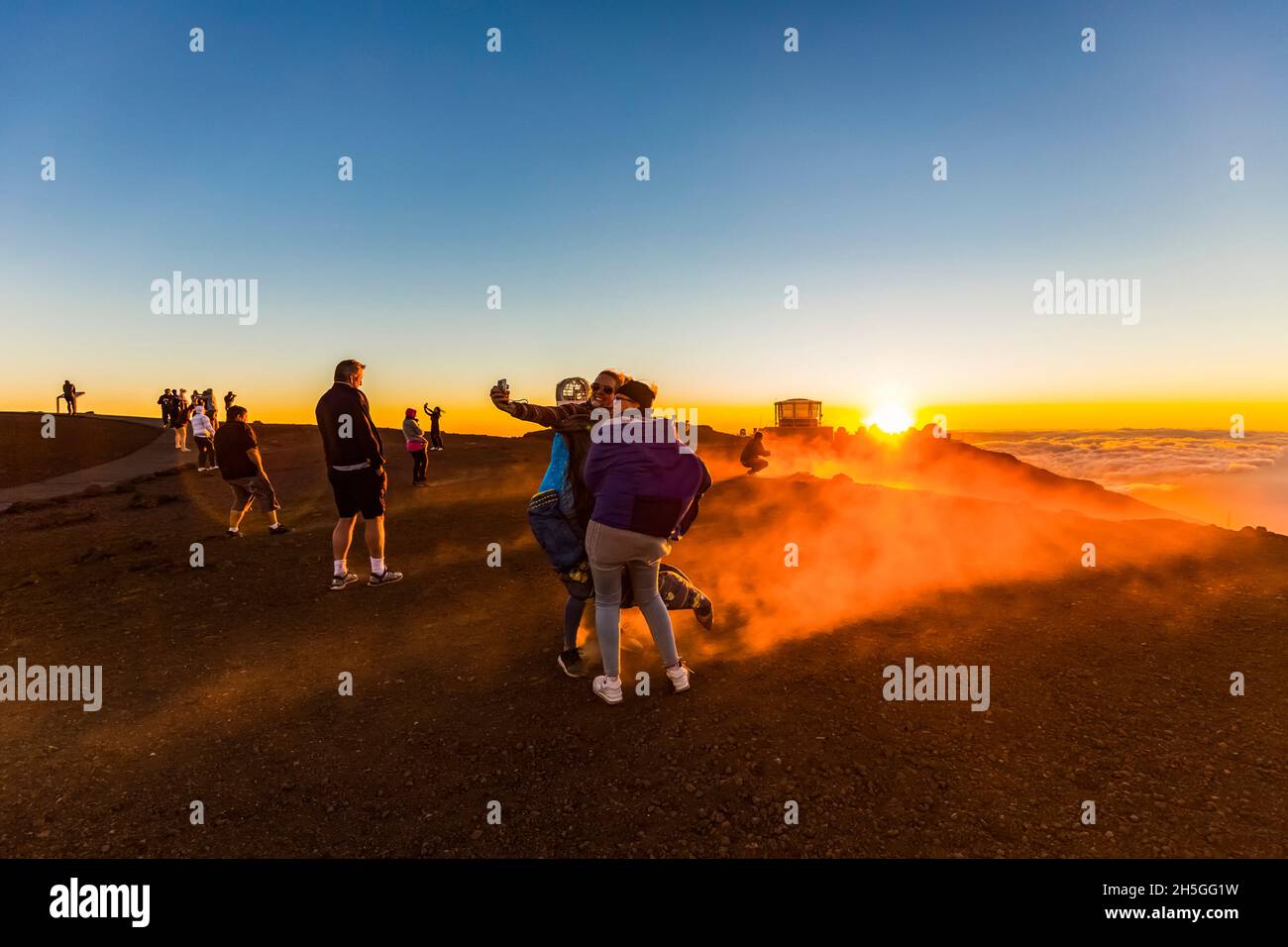 Touristen fotografieren und sehen die Gebäude des Haleakala Observatoriums über den Wolken bei einem farbenfrohen, dramatischen Sonnenuntergang; Maui, Hawaii, United Stat Stockfoto