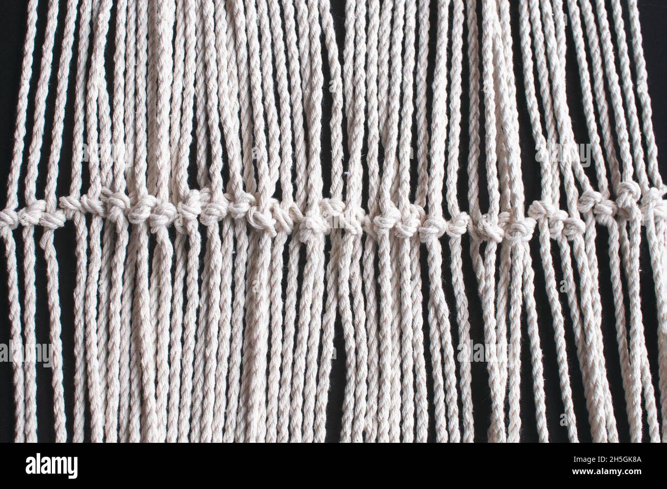 Makrames Ornament aus weißen Naturbaumwollfäden auf schwarzem Hintergrund. Handweberei aus Garn auf dunklem Grund Stockfoto
