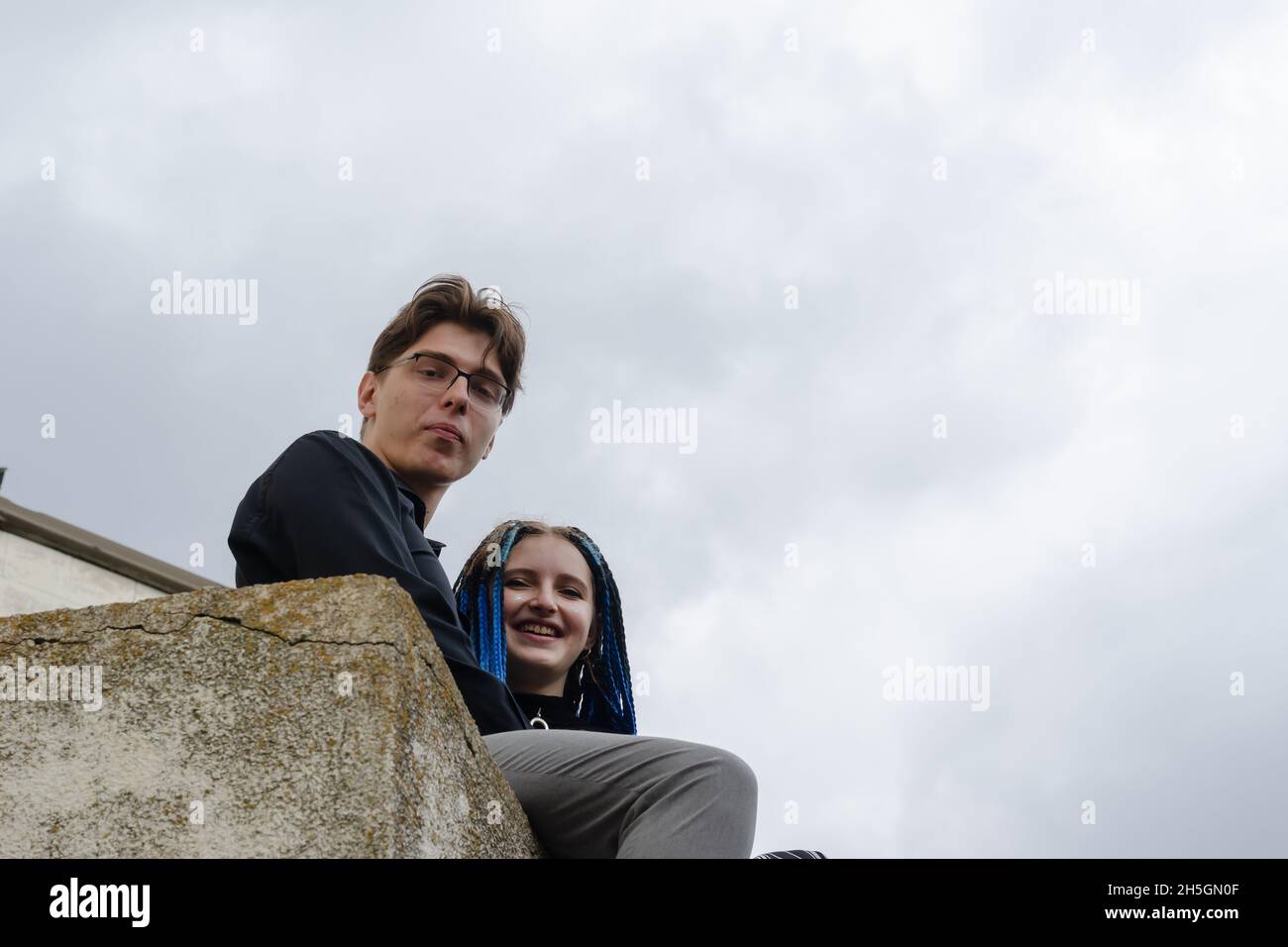 Ein Mann und eine Frau umarmen sich, sitzen auf einer Betonbrüstung. Die Frau ist lässig mit langen blauen Dreadlocks gekleidet. Mann in Geschäftskleidung. Blick vom Th Stockfoto