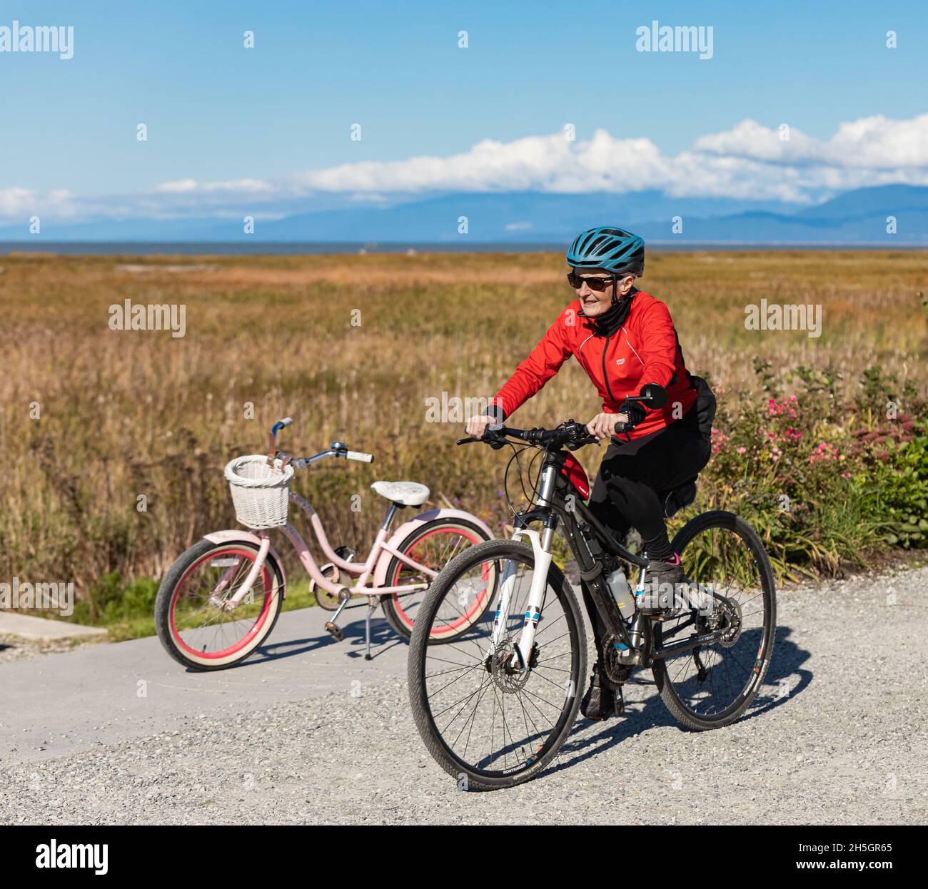Lächelnd fit ältere Frau auf einem Fahrrad in einem Park. Glückliche ältere Frau mit Helm auf dem Sportfahrrad. Straßenbild, Reisefoto, aktives Altern Stockfoto