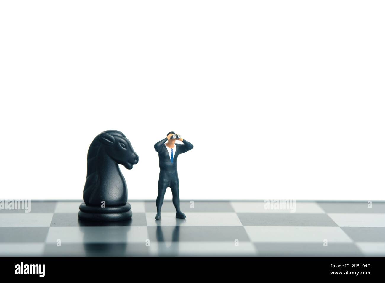 Geschäftsmann mit Fernglas, der neben dem Pferderitterschach steht. Miniatur winzigen Menschen Spielzeug Fotografie. Isoliert auf weißem Hintergrund. Stockfoto