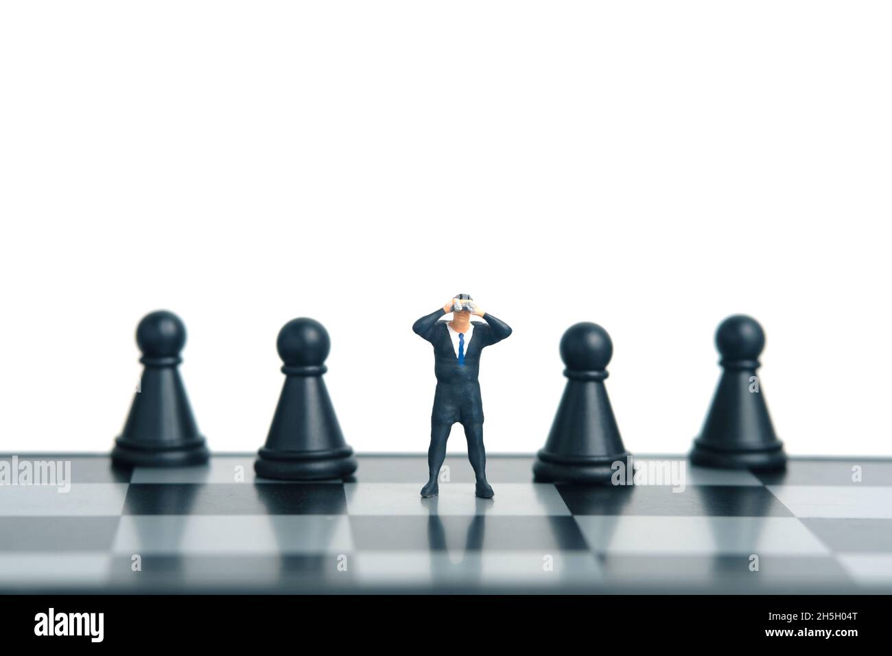 Geschäftsmann mit Fernglas, der zwischen dem Schachpfand steht. Miniatur winzigen Menschen Spielzeug Fotografie. Isoliert auf weißem Hintergrund. Stockfoto
