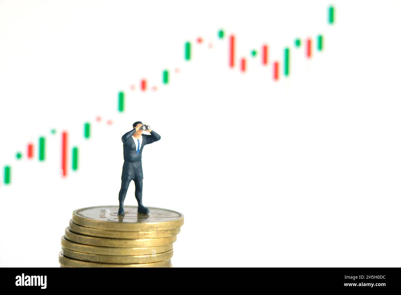 Geschäftsmann, der ein Fernglas über dem Münzstapel verwendet, mit einem bullischen Wachstum und einem Candle-Stick-Chart. Miniatur kleine Menschen Spielzeug Fotografie. Stockfoto