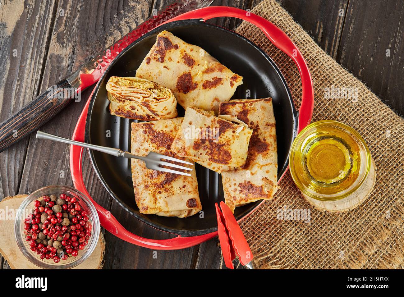 Pfannkuchen mit Fleisch auf Gabel mit Butter und Zange auf Teller auf dunklem Holzhintergrund Stockfoto