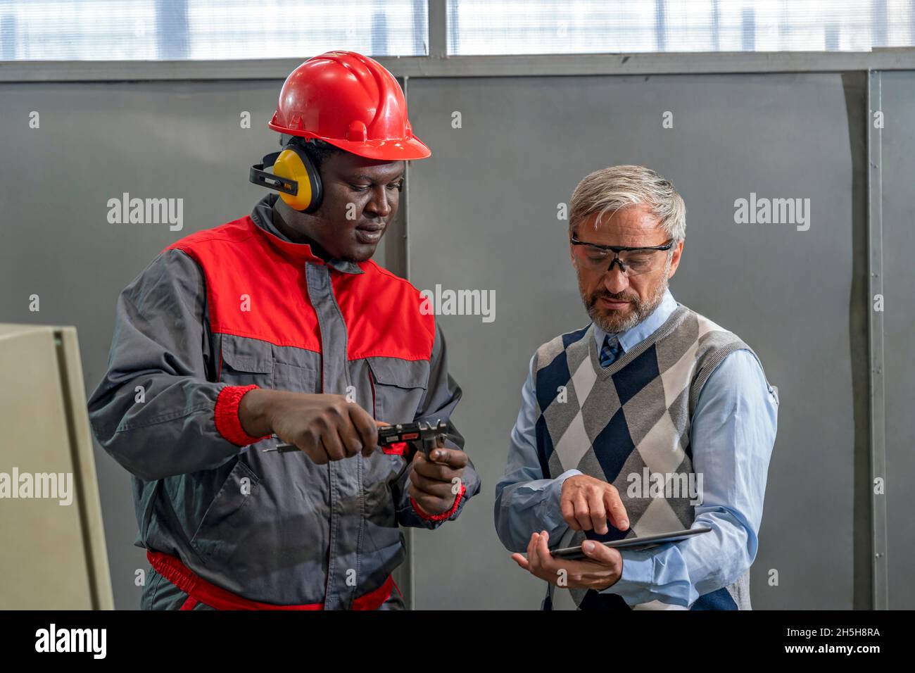 Multirassische Industrielle Mitarbeiter Stehen Und Reden Über Den Produktionsprozess. Schwarze Arbeiter Messen Mit Messschieber. Stockfoto