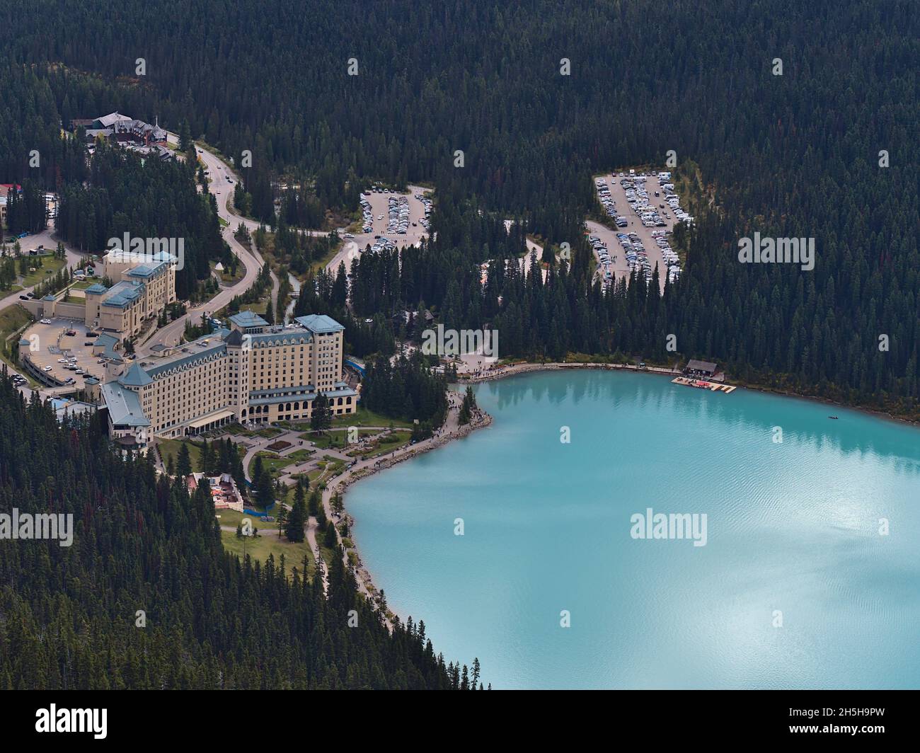Blick auf den östlichen Lake Louise mit türkisfarbenem Wasser, berühmtes Hotel und Parkplatz, umgeben von Wäldern im Banff National Park, Kanada. Stockfoto