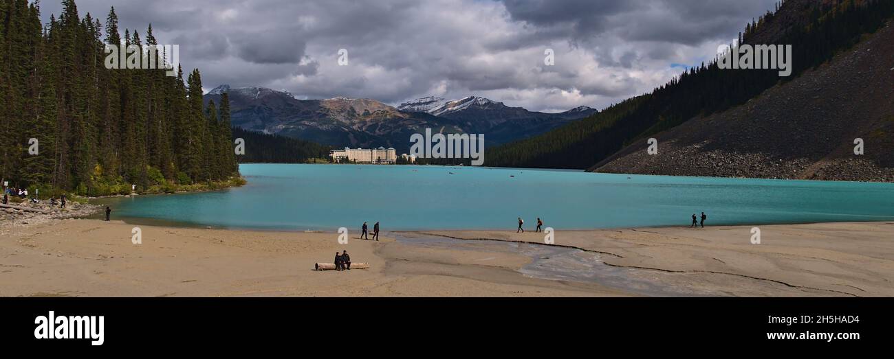 Panoramablick über Lake Louise mit türkisfarbenem Wasser, Touristen, die am Ufer spazieren und das Hotel in den Rocky Mountains im Banff National Park, Kanada. Stockfoto