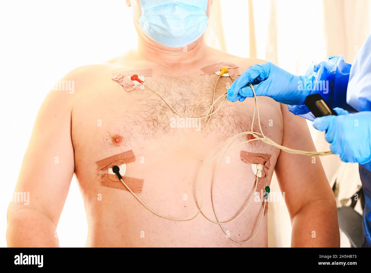 Der Arzt legt einen holter an die Brust des Mannes. Tägliche Überwachung des Herzens. Kardiologie. Stockfoto