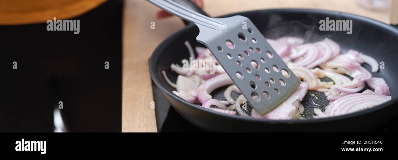 Frau frittiert Zwiebeln in Pfanne in der Küche Nahaufnahme Stockfoto