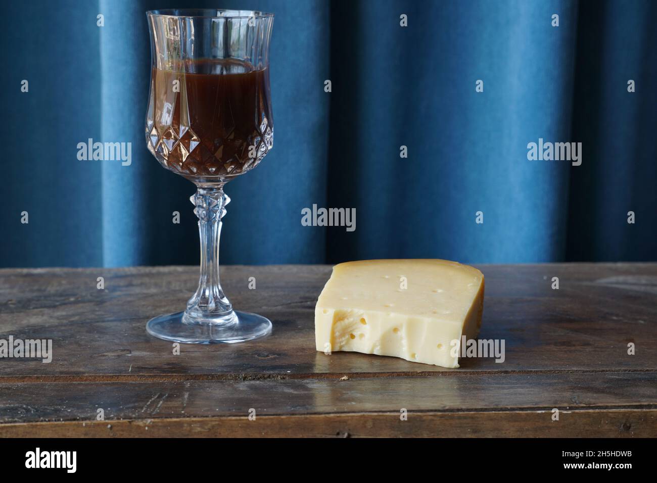 Cheddar-Käsestück auf einem Holztisch neben einem Weinglas Stockfoto