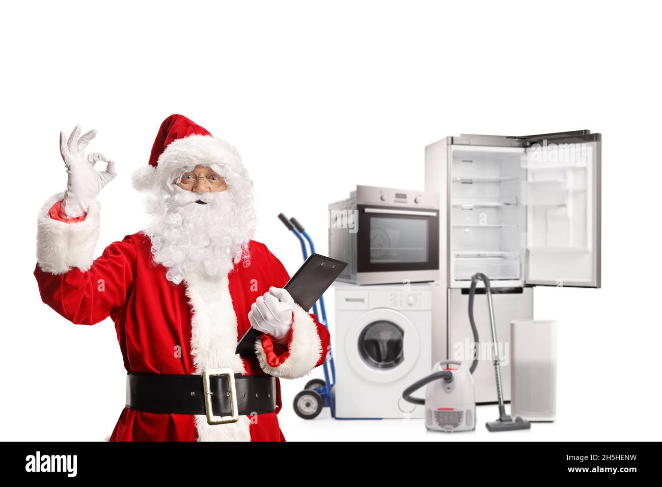 Der weihnachtsmann hält eine Zwischenablage und deutet ein gutes Zeichen vor Haushaltsgeräten, die auf weißem Hintergrund isoliert sind Stockfoto