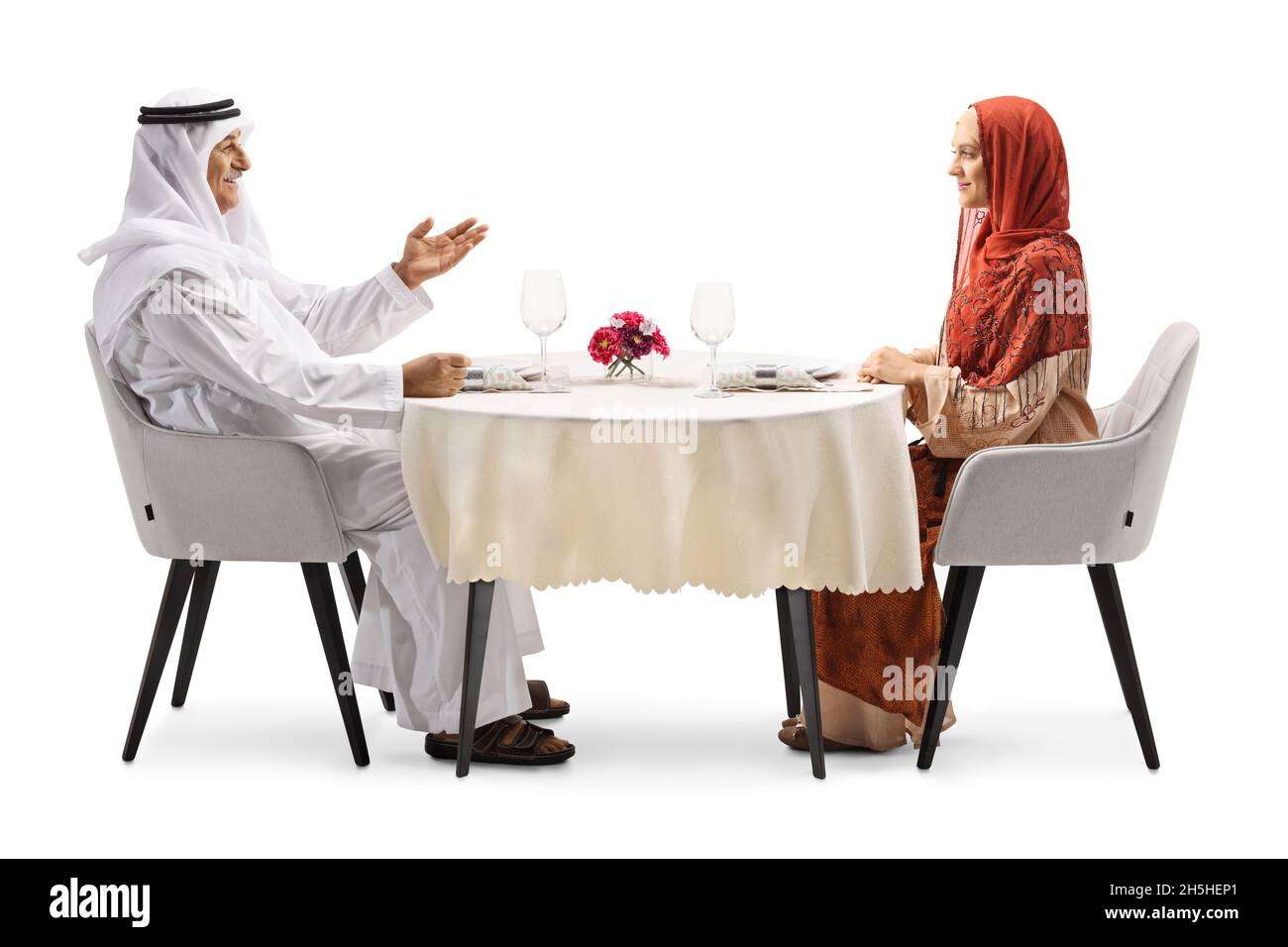 Arabischer Mann im Gespräch mit einer Frau in einem Hijab, der an einem Restauranttisch auf weißem Hintergrund sitzt Stockfoto