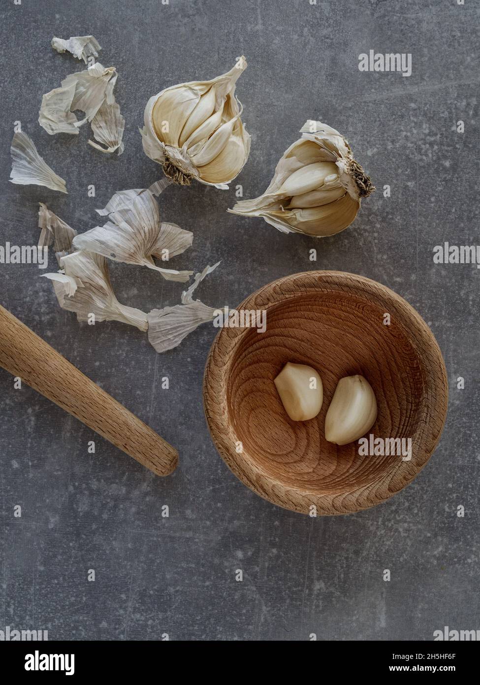 Knoblauchzwiebeln (Allium) und Küchenmörtel aus Holz auf Betongrund. Aufnahme über Kopf. Speicherplatz kopieren. Stockfoto