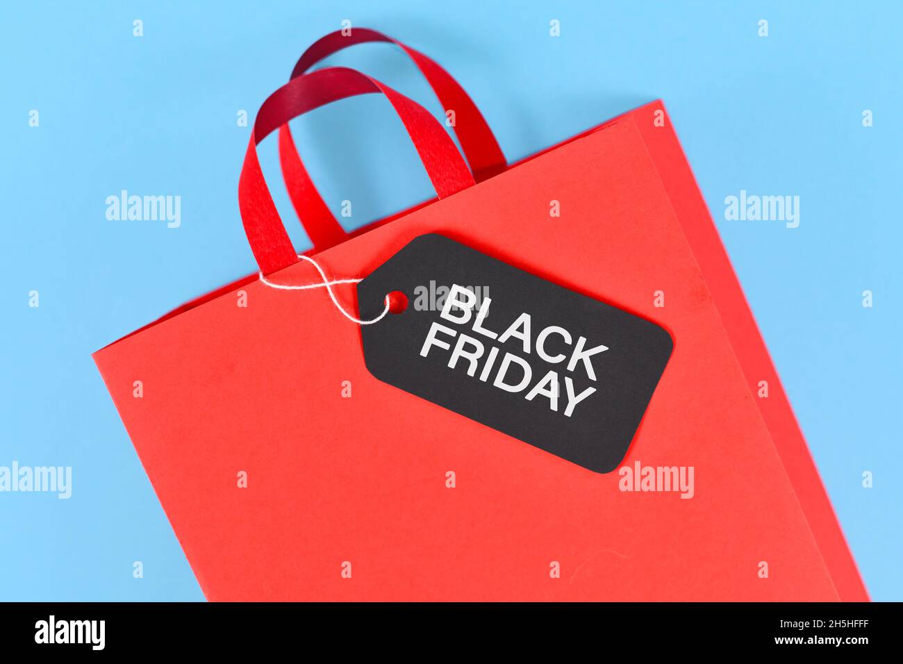 Schwarzes Freitagsetikett auf roter Papier-Einkaufstasche auf blauem Hintergrund Stockfoto