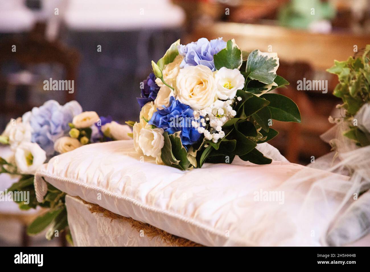 Farbenfroher Brautstrauß aus weißen und blauen Blumen, der auf Kissen über der Hochzeitsbank vor dem Kirchenaltar liegt Stockfoto