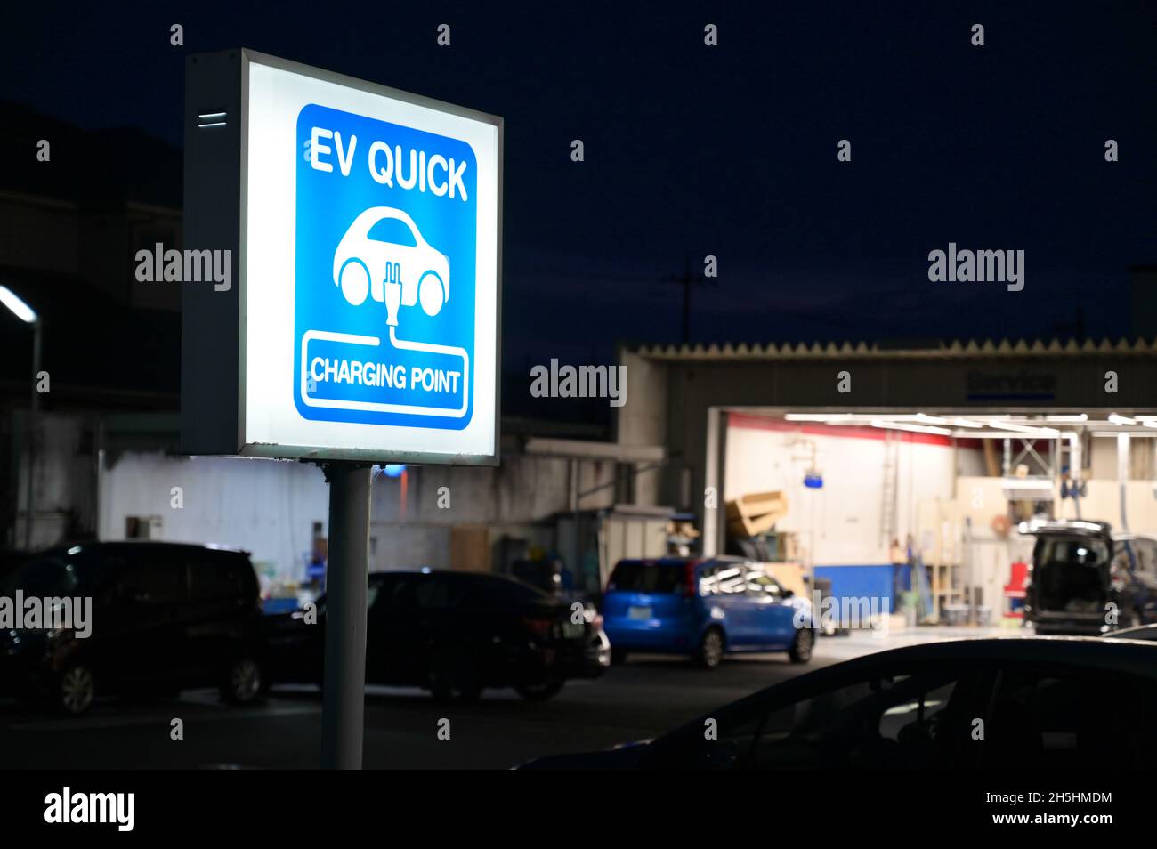 EV Schnellladestelle für Elektrofahrzeuge. Blaues Leuchtzeichen. Werkstatt im Hintergrund. Stockfoto